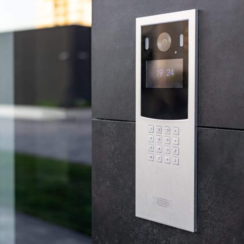 Entrance doorbell in a multi-apartment building, with a video surveillance camera, on a dark wall